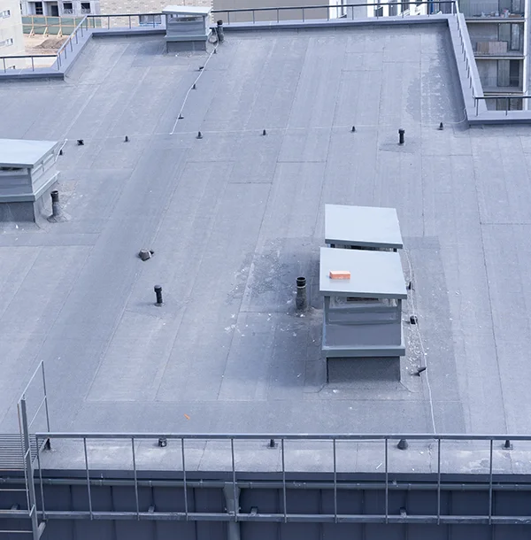 Flat membrane roof seen from above with vent pipes, two rooftop units and a metal railing