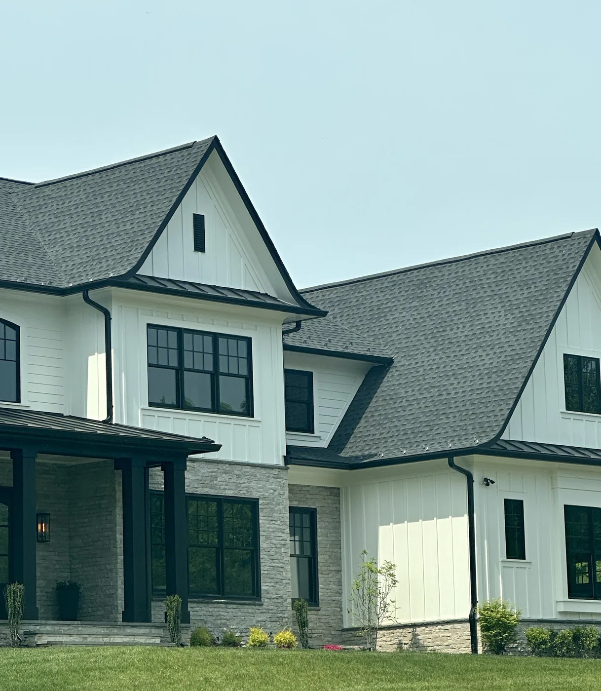 Two-story white house with a dark gray shingle roof, metal porch roofs and black gutters