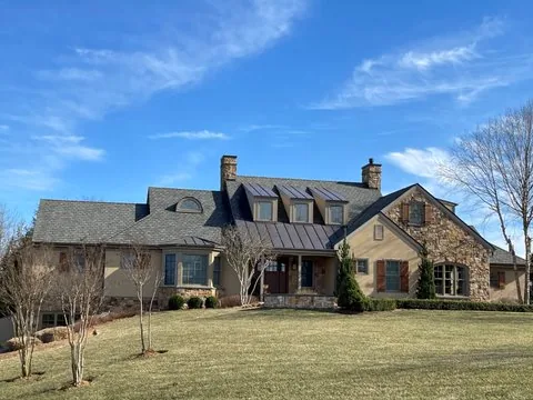 Large stone and stucco house with a gray shingle roof and a standing seam metal entry roof